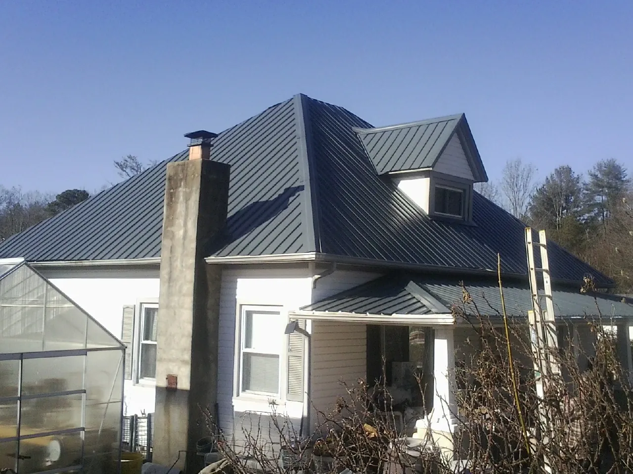 Dark blue standing seam metal roof on a white farmhouse with dormer — Slate & Tile Roof Repair by Roofing Brothers in Big Lake