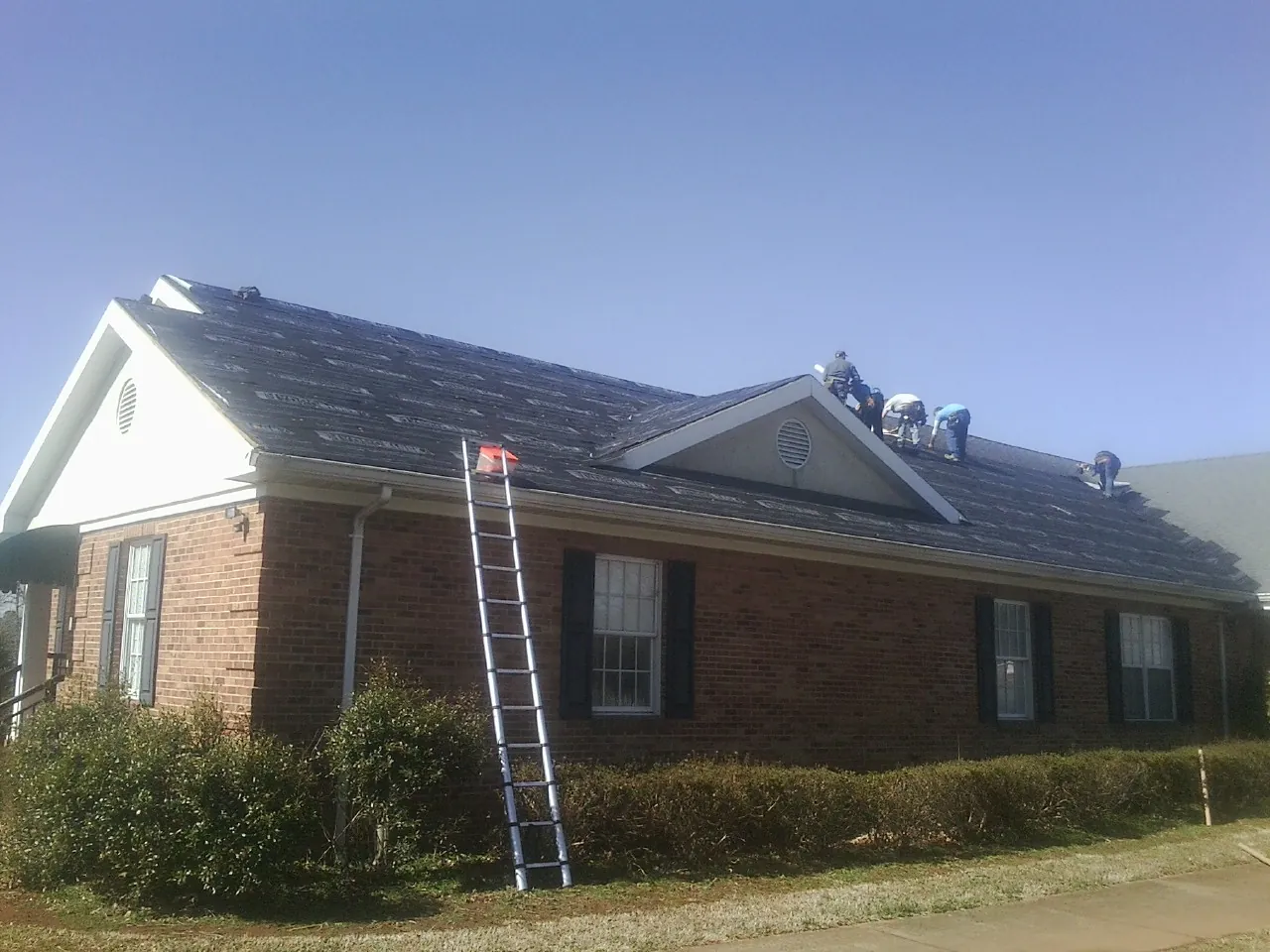 Crew tearing shingles off a brick ranch roof with a ladder set — Metal Roof Repair work by our crew in Big Lake
