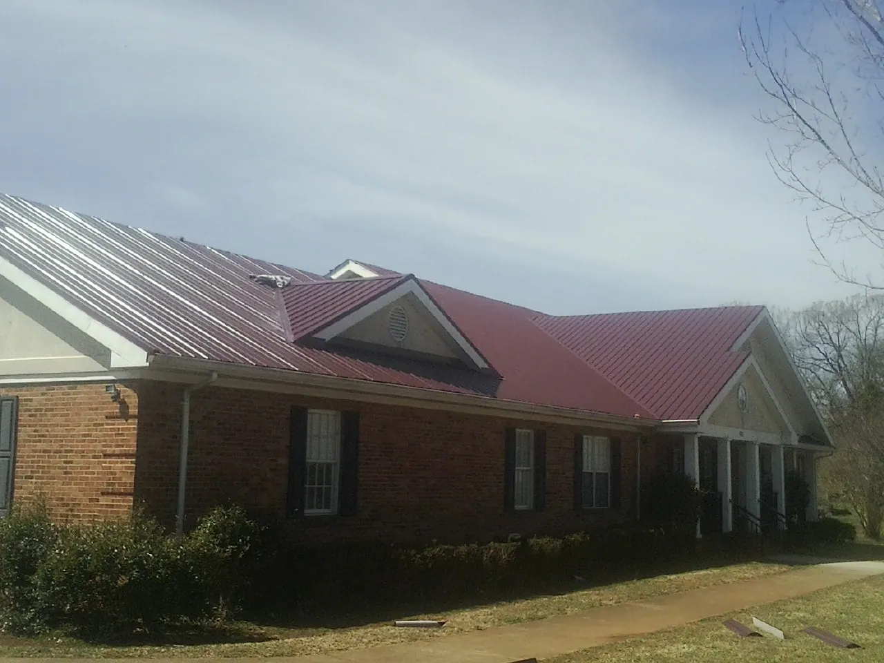Red metal roof with gabled entries on a long brick building, from a Hail Damage Roof Repair job in Big Lake