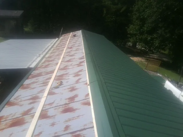 Old rusted panels beside newly installed green metal roofing — Wind Damage Roof Repair by Roofing Brothers in Big Lake