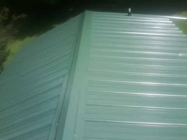 New green metal panels meeting at the ridge of a roof — Flat Roof Repair work by our crew in Big Lake