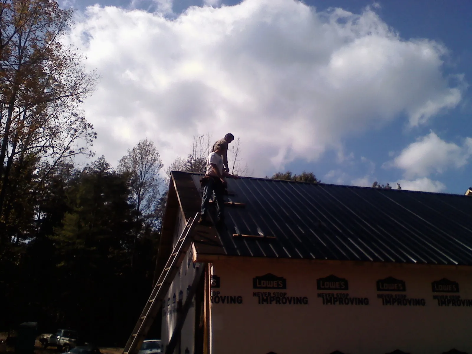 Roofer fastening dark metal panels high against a cloudy sky, from a Roof Inspection job in Big Lake