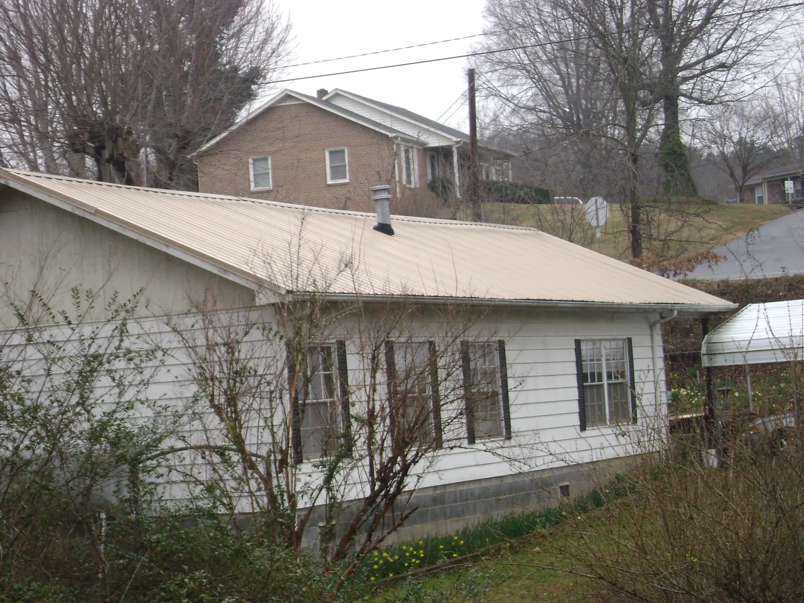 Tan metal roof on a white sided house set into a hillside — Commercial Roofing by Roofing Brothers in Big Lake
